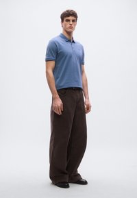 Gaiši zils polo krekls ar īsām piedurknēm, kopā ar brūnām platām biksēm. Apģērbu papildina melni apavi.