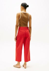 Czerwone spodnie szerokie na nogawkach wykonane z bawełny, z wysokim stanem, dwiema tylnymi kieszeniami i luźnym krojem. W komplecie z brązowym topem bez rękawów.