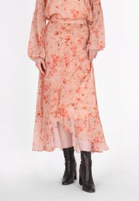 Blumengemusterter, Faltenrock in Pfirsichtönen, mit asymmetrischem Saum und leichtem, transparentem Stoff. Kombiniert mit schwarzen Chelsea-Boots.