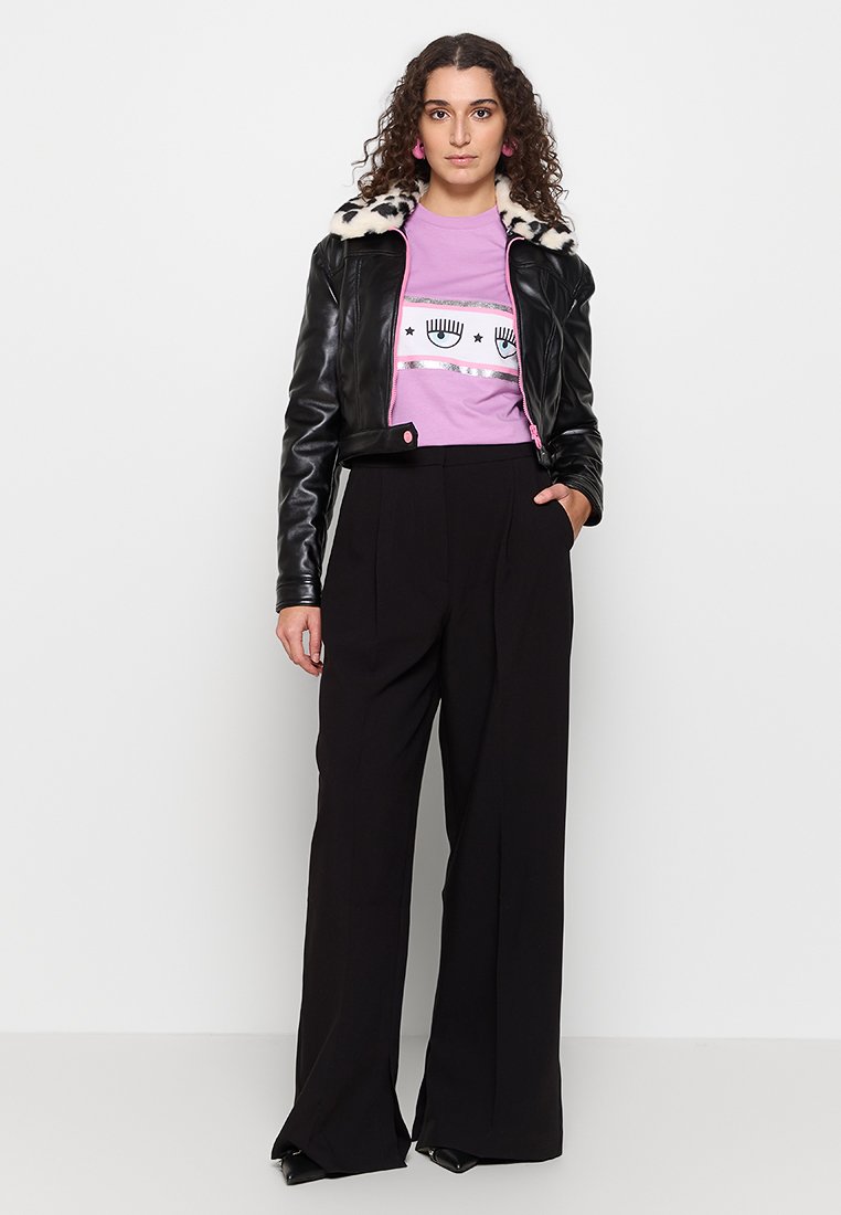 Schwarze Lederjacke mit einem Kunstfellkragen, lila Grafik-T-Shirt und lockeren schwarzen Hosen mit Falten und weitem Bein.