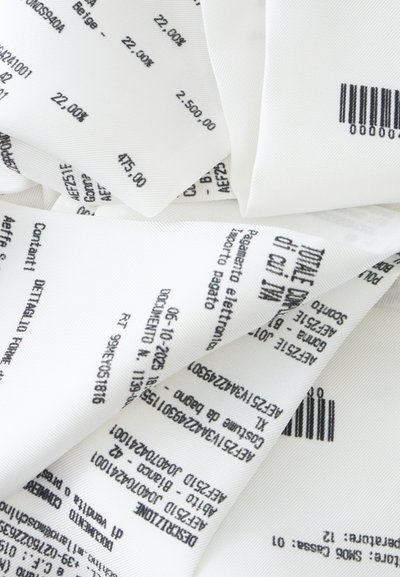 Étiquettes en tissu blanc avec texte noir imprimé, chiffres, codes-barres et détails du produit, superposées et pliées étroitement.