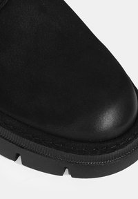 Bottes chevilles en cuir noir avec un bout arrondi, une surface mate texturée et une semelle en caoutchouc épaisse avec des accents rainurés.