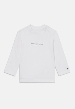 Bijela baby majica dugih rukava s "Tommy Hilfiger EST. 1985" logotipom na prsima i malim logotipom zastave na manžetni lijevog rukava.