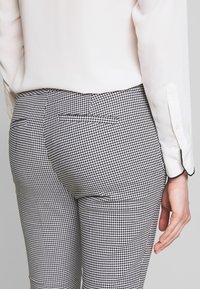 Svart och vit houndstooth-mönstrade byxor med slim fit, med två bakfickor och en slät tygkvalitet.