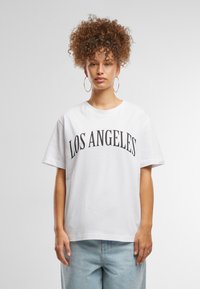 T-shirt en coton blanc portant "LOS ANGELES" en lettres noires en gras et courbes. Manches courtes et coupe décontractée. Bas en denim bleu clair.