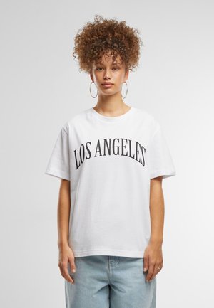 T-shirt en coton blanc portant "LOS ANGELES" en lettres noires en gras et courbes. Manches courtes et coupe décontractée. Bas en denim bleu clair.