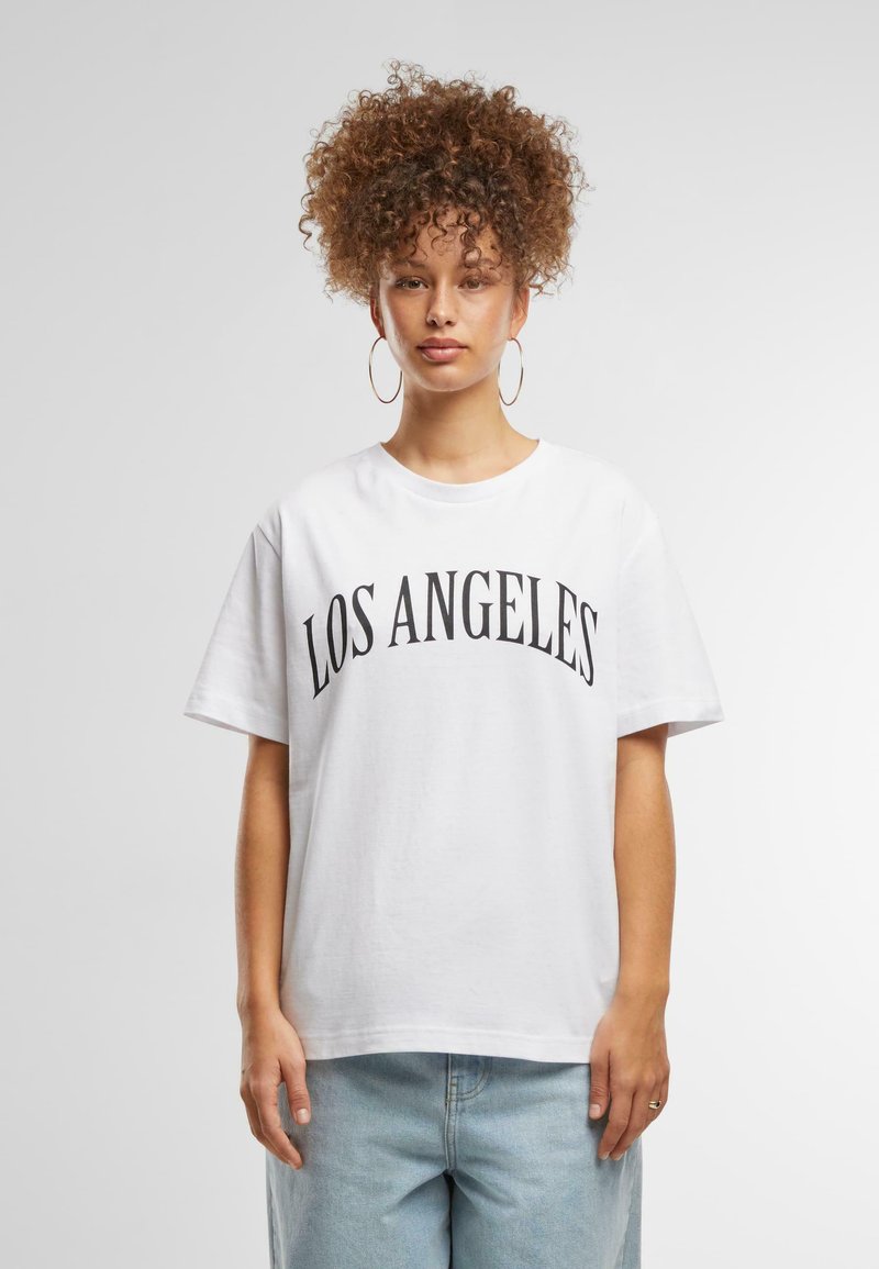 T-shirt en coton blanc portant "LOS ANGELES" en lettres noires en gras et courbes. Manches courtes et coupe décontractée. Bas en denim bleu clair.