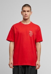 Rød bomull t-skjorte med kort erme og rund hals, med grafisk trykk i svart og hvitt på venstre side.