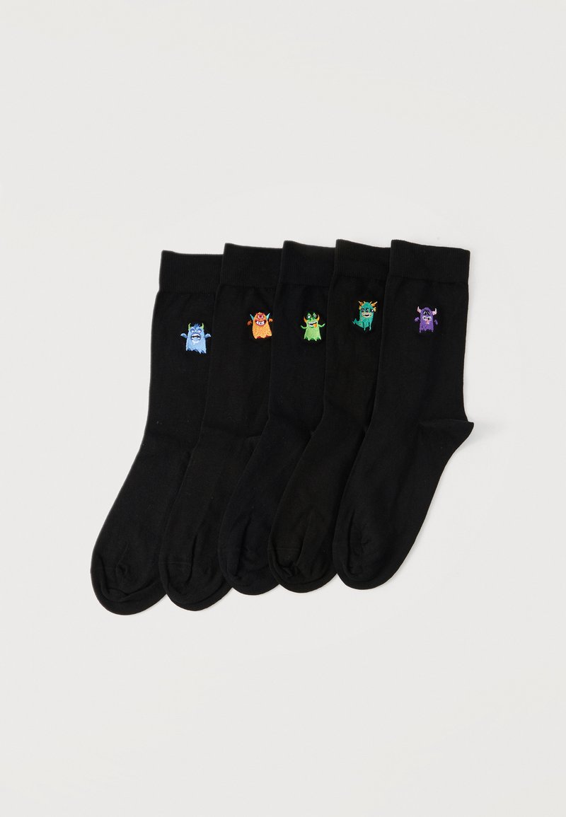Cinq chaussettes noires étalées à plat, chacune avec un petit monstre coloré brodé près du haut du bord en bleu, orange, vert, bleu sarcelle et violet.