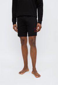 Μαύρο σορτς από μαλακό υλικό, με κόκκινη καρδιά και το κέντημα "HUGO" κάτω αριστερά, με χαλαρή εφαρμογή.