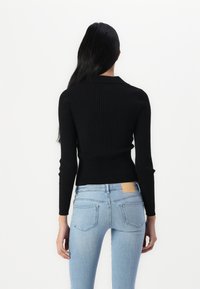 Black ribbed sweater with a fitted design and long sleeves, paired with light blue denim jeans featuring back pockets.