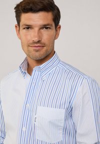 Camicia a righe con righe sottili blu e bianche, dotata di una tasca sul lato sinistro, realizzata in un tessuto morbido.