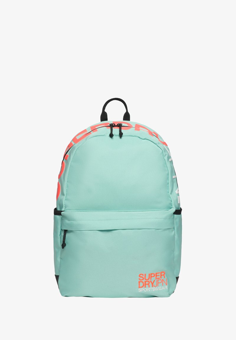 Mochila de color turquesa claro con bolsillo frontal y asa negra, que presenta el logotipo en rojo y blanco "Superdry JPN Sportswear" en la parte frontal y los laterales.
