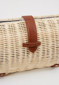 Woven straw bag with a brown leather strap. Rectangular shape, light beige color, featuring a smooth texture and stitched accents.