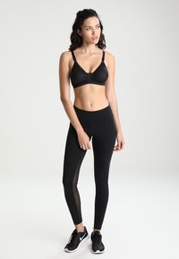 Svart sportsbh med justerbare stropper, parret med svarte tights med gjennomsiktige sidepaneler. Begge laget av pustende, elastisk materiale.