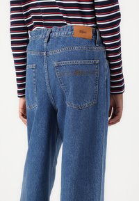 Lyseblå denimjeans med avslappet passform, med baklommer, en brun skinnlapp i livet og en subtil brodert logo.