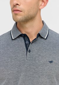 Szara koszulka polo z teksturowanej tkaniny, granatowym kołnierzykiem z białym wykończeniem, zapięciem na trzy guziki oraz małym czarnym emblematem na piersi.