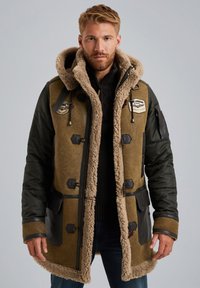 Bruine en groene parka van dubbele materialen met een met bont gevoerde capuchon, zwarte accenten, meerdere voorzakken en een ritssluiting.