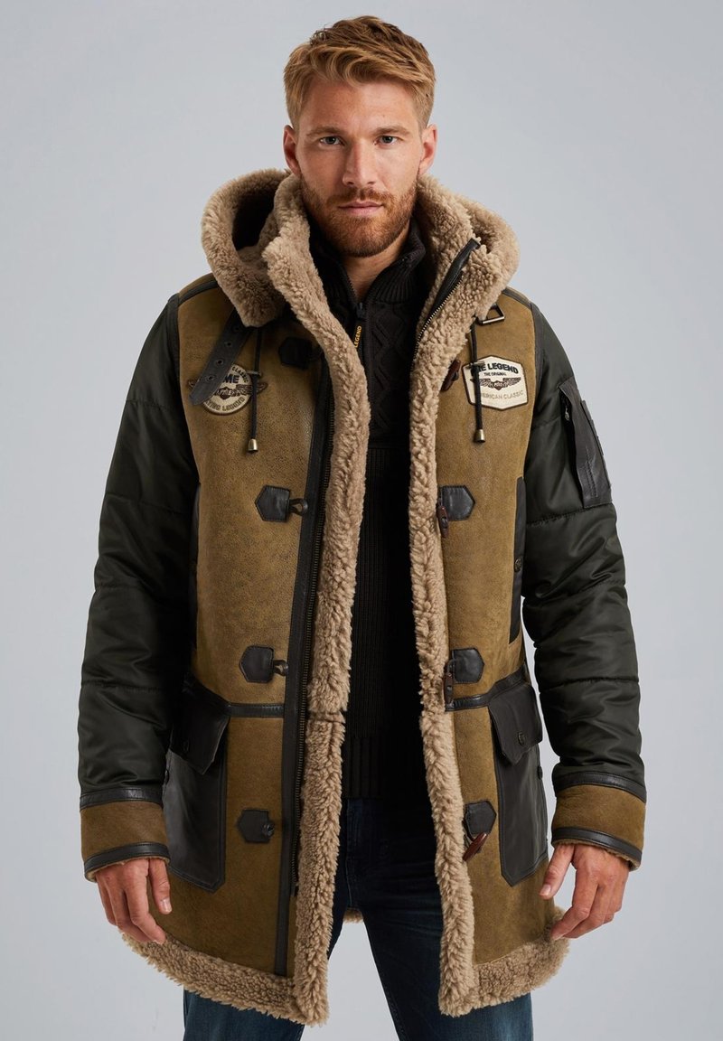 Bruine en groene parka van dubbele materialen met een met bont gevoerde capuchon, zwarte accenten, meerdere voorzakken en een ritssluiting.