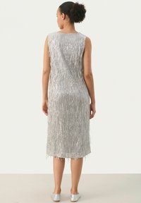 Silbernes ärmelloses Kleid mit vertikalem Fransen-Design, mittellanger Schnitt, glatter Textur und rundem Halsausschnitt. Tragen mit silbernen Ballerinas.