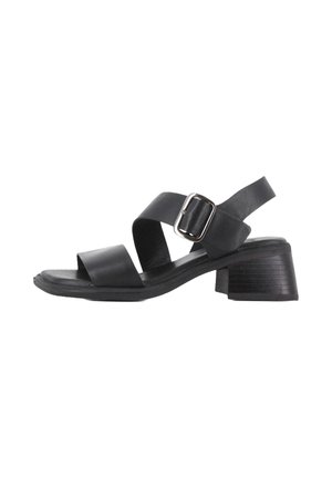 Sandalia de cuero negro con dos correas anchas y un hebilla lateral, que presenta una suela de tacón grueso y un diseño de punta plana.