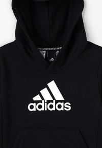 Czarna bluza z kapturem wykonana z bawełnianej mieszanki materiałów. Posiada duże białe logo Adidas na przodzie oraz kieszeń kangurkę na dole.