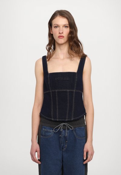 Tmavě modrý denimový cropped top s širokými ramínky, čtvercovým výstřihem a centrálním logem. Kontrastní prošívání zvýrazňuje detaily panelů.