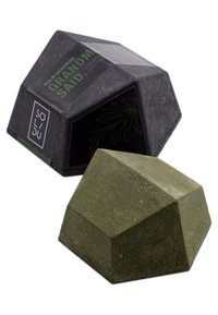 Stały szampon w geometrycznym kształcie, zielony kolor z fakturowaną powierzchnią, zapakowany w czarne pudełko z zielonymi akcentami i logo.