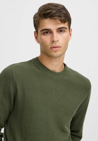 Groene gebreide trui met textuur en ronde halslijn, met een iets getailleerde vorm en een subtiel patroon door het hele doek.