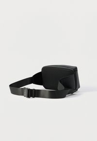 Μαύρη τσάντα μέσης με πίσω πάνελ από δίχτυ και ρυθμιζόμενο λουρί νάιλον με πλαστική αγκράφα, τοποθετημένη σε απλό λευκό φόντο.