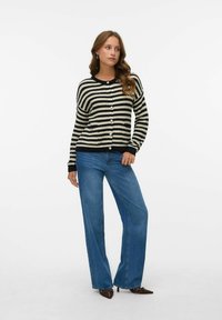 Zwart en crèmekleurige gestreepte cardigan met knopen en geribde manchetten, gecombineerd met een wijde jeans in blauw en bruin puntig-schoeisel.