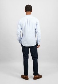 Camicia azzurro chiaro a maniche lunghe con polsini a bottone, abbinata a pantaloni scuri e mocassini marroni. Tessuto liscio, vestibilità casual, orlo arcuato.