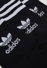 Black cotton socks featuring three white stripes at the top and Adidas logo with a trefoil design, structured knit texture.
