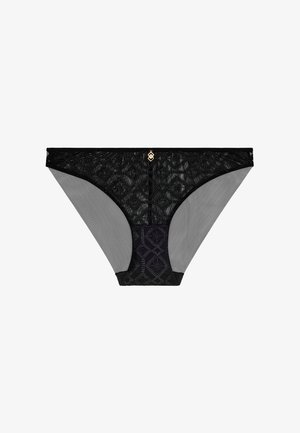 Tanga en dentelle noire avec côtés en mesh gris transparent, présentant un motif géométrique à l'avant et un emblème doré au centre. Tissu texturé.