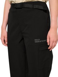 Prim-plan cu pantaloni negri cu curea încorporată, buzunar lateral și text reflectorizant "HALO 196819721981" pe coapsă.