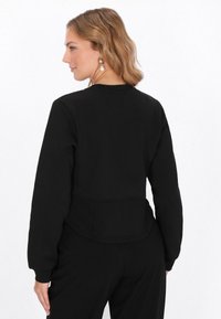 Fekete, rövidített pulóver hosszú ujjakkal, kerek nyakkivágással és szabott derékrésszel. Sima anyag, hátul varrással, amely vizuális érdekességet kölcsönöz.