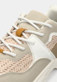 Baskets beige et blanches avec un tissu rose tissé, un daim lisse, des lacets blancs et une boucle d'accent brun. Bout arrondi et semelle texturée.