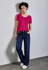 T-shirt fucsia a maniche corte con scollatura tonda, abbinato a jeans a gamba larga blu scuro a vita alta e sneakers bianche.