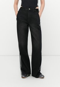 Svarta vida byxor med en denimframsida och släta svarta tygsidor, accentuerade med tre vita ränder och fickor.