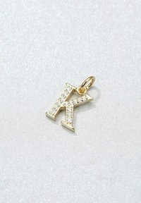 Charm en forme de lettre "K" plaqué or avec de petites pierres précieuses claires incrustées sur le devant, boucle pour attache, finition brillante.
