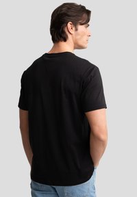 Schwarzes Baumwoll-T-Shirt mit kurzen Ärmeln, Rundhalsausschnitt und einem dezenten Nahtdetail auf der Rückseite. Fällt locker am Körper.