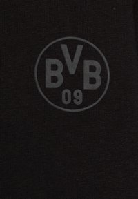 Svart tyg med en rund, präglad logotyp med bokstäverna "BVB" och "09" i centrum. Texturen är slät med ett subtilt stickat mönster.