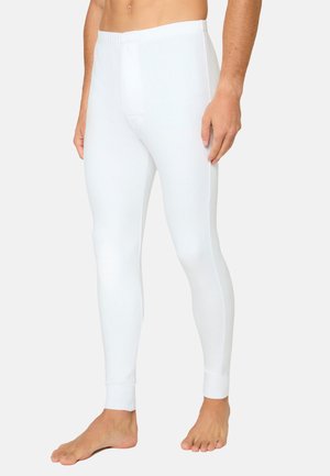 Man wearing plain white fitted thermal leggings standing barefoot on a light background.
