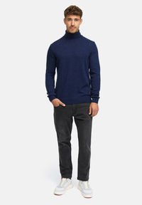 Navyblauer Rollkragenpullover in einer Stricktextur, kombiniert mit dunkelgrauen Jeans und hellen Sneakers, was ein entspanntes Outfit ergibt.