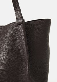 Sac en cuir marron avec une surface texturée, doté d'une large ouverture et d'une bandoulière robuste. Pas de quincaillerie ou d'accents visibles.