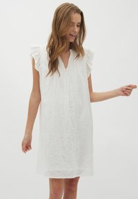 Weißes Leinenkleid mit V-Ausschnitt, kurzen Rüschensäumen und lockerer Passform. Verfügt über dezente vertikale Falten für Textur und Detail.