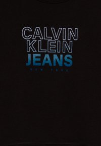 Crna majica s kapuljačom s natpisom "CALVIN KLEIN JEANS" u podebljanim, gradijentnim slovima od bijele do plave, s "NEW YORK" ispisanim ispod u manjem fontu.