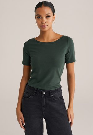 Groene T-shirt met korte mouwen, gemaakt van zachte stof en met een ronde halslijn. Gecombineerd met hoge zwarte jeans, met een klassieke denimtextuur.