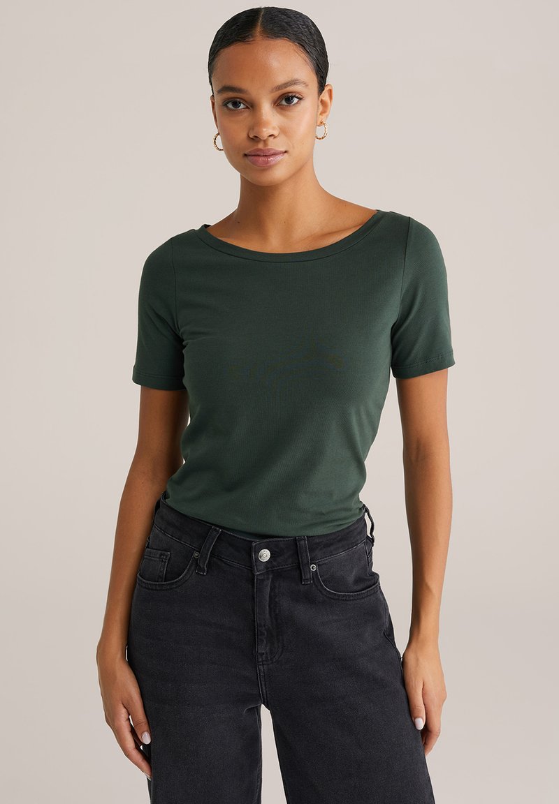 Zaļa īsu piedurkņu T-kreklu, kas izgatavots no mīksta auduma ar apaļu kakla izgriezumu. Apvienots ar augsto jostasvietu melnām džinsu biksēm, kurām ir klasiskā džinsu tekstūra.