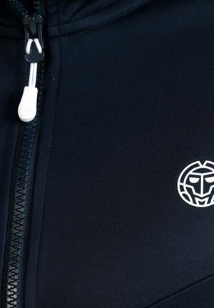 Close-up van zwarte stof met een wit plastic ritslipje en een wit cirkelvormig logo met een gestileerd gezicht.